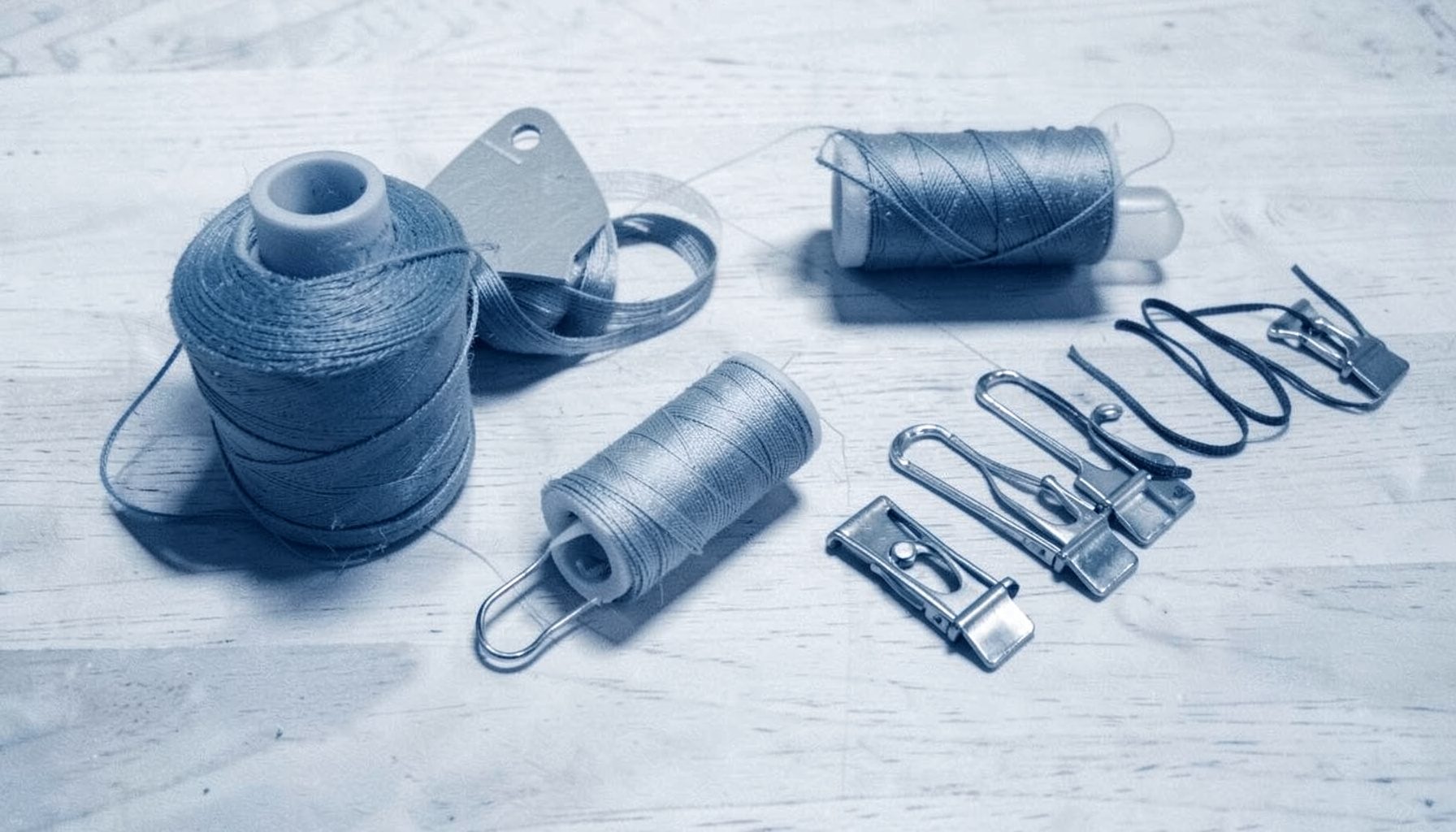Spools of thread, elastic bands, and sewing clips arranged neatly on a light wood tabletop