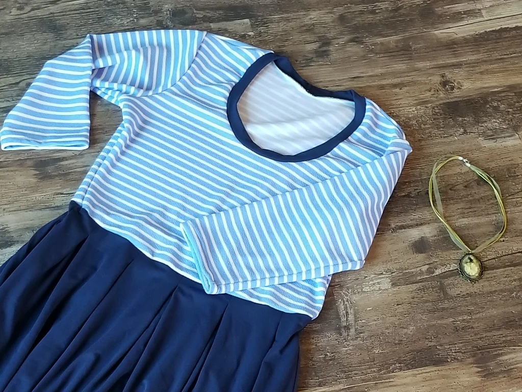 Blue and white striped top with navy skirt laid flat on wood floor, necklace beside it