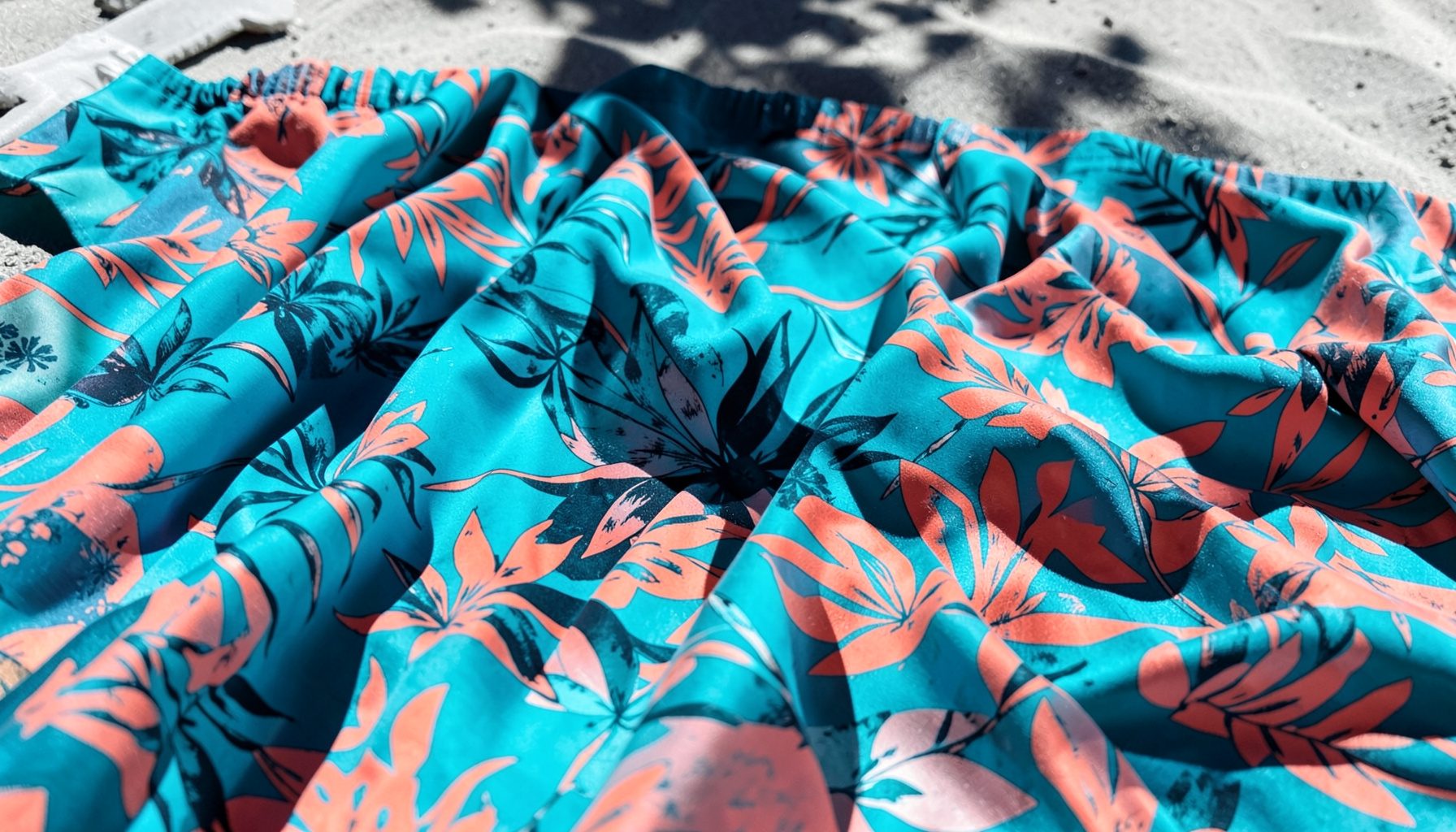 Vibrant tropical-print swim fabric in turquoise and coral tones draped across a sunlit surface