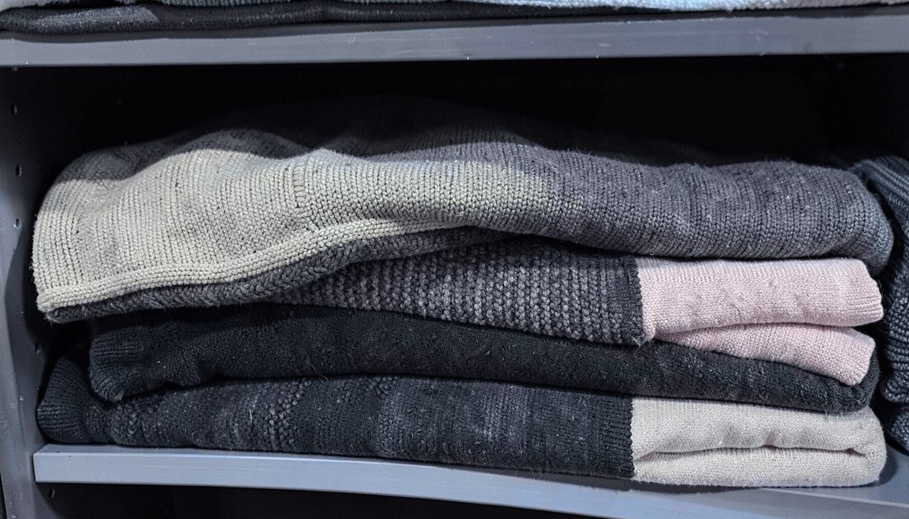 Rolls of sweater knit fabric in oatmeal, charcoal, and blush tones stacked on shelving