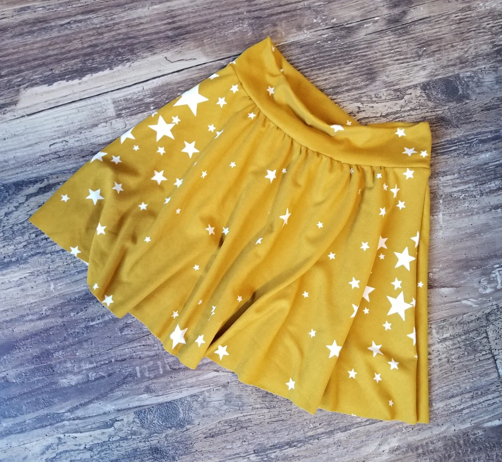 Mustard yellow skater skirt with white star print laid flat on a wooden floor