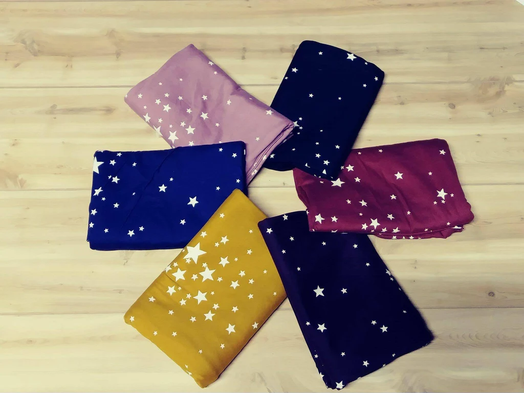Six folded star-patterned fabric pieces in various colors arranged in a circle on wood surface